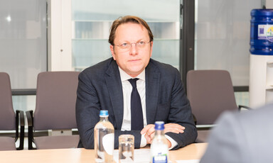 Olivér Várhelyi, a member of the European Commission, sits at a desk with a glass and bottles of water