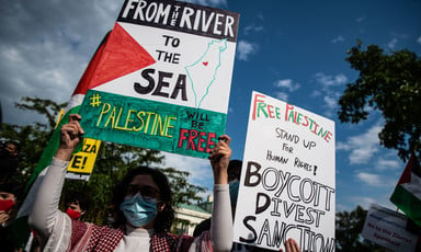 Protesters hold signs above their heads, one calling for boycott, divestment and sanctions against Israel and the other calling for Palestine to be free from the river to the sea.