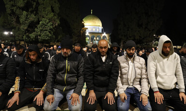 A group of mean kneels in prayer with golden dome behind them