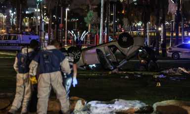 Men in hazmat suits stand near overturned sedan in nighttime scene