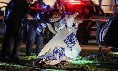 Officers, one wearing a hazmat suit, lift tarp over body lying on ground