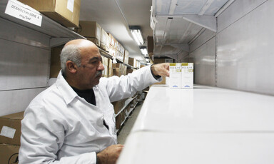 A pharmacist wearing a white coat stands next to a shelf with very few medicines in a Gaza warehouse 