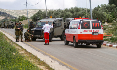 Palestinian paramedic raises his hand to group of Israeli soldiers while standing next to ambulance and in front of military jeep