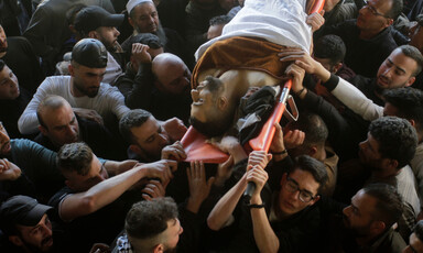 A group of men are seen carrying a stretcher with the body of a man covered in a white sheet