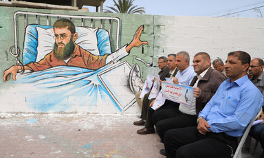 Men are seated near a mural that depicts a prisoner in a hospital bed 