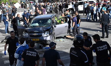 A battered SUV in a crosswalk is surrounded by police, first responders and onlookers