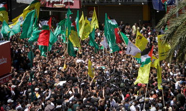 A crowd of hundreds fly faction flags as two shrouded bodies are carried on stretchers