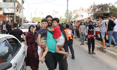 A man holds two young boys in his arms as people gather in street