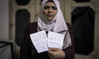 Woman wearing a white headscarf holds two pieces of paper in one hand