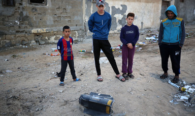 Four children stand near and observe an exploded missile on the ground 