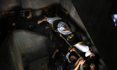 People carry a corpse wrapped in a flag down a staircase 