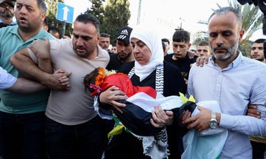 Woman holds body of toddler shrouded in Palestine flag in funeral march