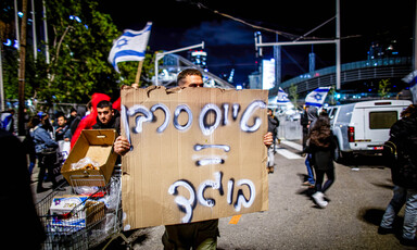 A man holds a hand-written sign in Hebrew