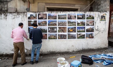 Two men put up photos on a white wall