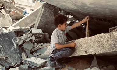 A boy sits amid the rubble of a building that has been destroyed 