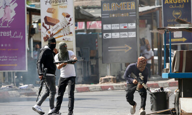 Three men wearing street clothes with their faces covered carry rifles in street