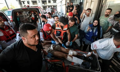 Journalists hold up cameras as paramedics push a stretcher carrying a man with bandaged legs