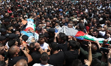 A crowd of dozens carry two bodies on stretchers wrapped in Palestine flags and kuffiyehs