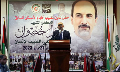 A man stands on a podium with a large photographic tribute to the dentist Jamal Khaswan behind him