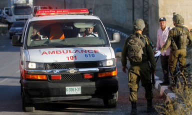 Soldiers seen from back stand in front of ambulance with two medics sitting in the front