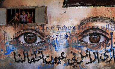 A mural in Gaza city depicts a closeup of realistic eyes as children peek out from a window embedded in the mural