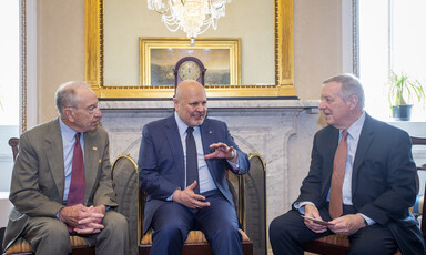 Grassley, Khan and Durbin sit in chairs in front of mirror reflecting chandelier