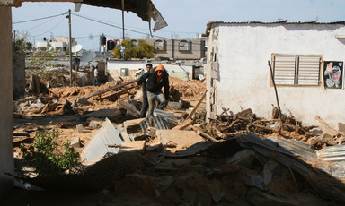 Two young men walk beside a building with much debris on the ground 