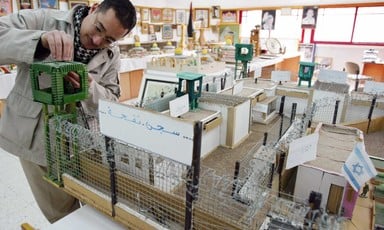 A man stands near a small replica of the Israeli Nafha prison, complete with miniature barbed wire and a guardpost.