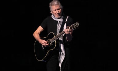 The musician Roger Waters wears a black and white checkered scarf while playing guitar onstage