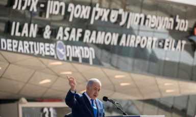Israel's Prime Minister Benjamin Netanyahu speaks at a podium. Above him are signs reading "Departures" and "Ilan & Asaf Ramon Airport - Eilat." 