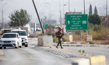 Soldier carrying rifle walks on median with Palestinian-plated cars in one lane and an empty lane on the other side