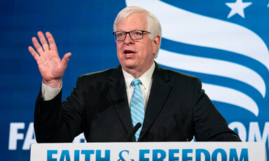 Dennis Prager raises his hand at podium before a faith and freedom sign