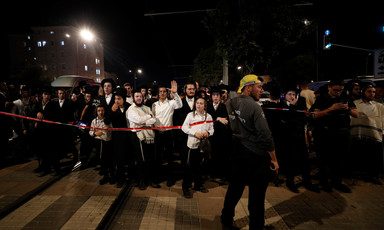Men and boys in Orthodox Jewish dress stand behind police tape at night