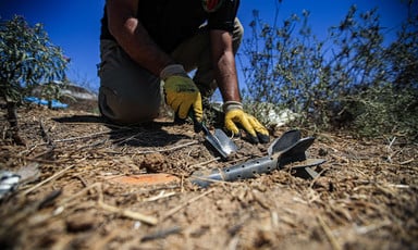 A close-up photograph of an EOD team member with a small shovel digging around a piece of ordnance.
