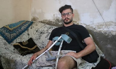 Muhammad Hussein sits on a couch with his forearm canes resting near his amputated leg.
