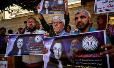 People stand shoulder to shoulder on a sidewalk carrying signs with the face of Elizabeth Tsurkov on them