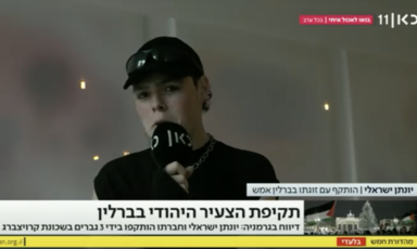 Still from video of man in baseball cap holding microphone speaking to TV news show