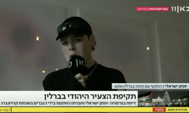 Still from video of man in baseball cap holding microphone speaking to TV news show