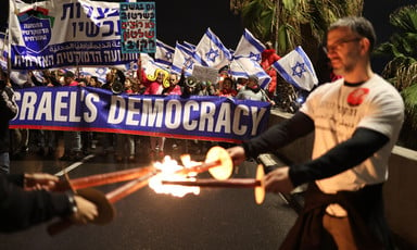 At nighttime, Israelis hold Israeli flags and a banner reading "Democracy."