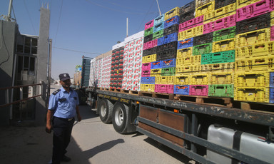 Man in uniform stands next to trailer bed loaded high with boxes and crrates