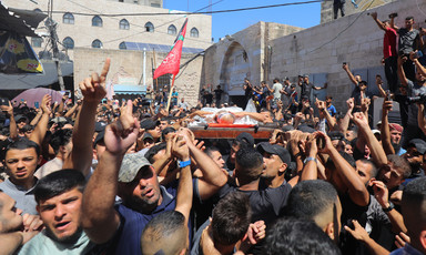 Crowd of men carry shrouded body on stretcher