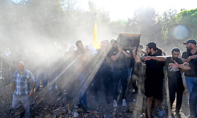 Sunlight streams over the shoulders of young men carrying a coffin