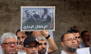 Men stand in demonstration, one of them holds a poster that says "no to administrative detention" 