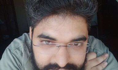 Portrait of a man with dark hair and beard and wearing glasses 