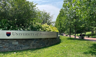 A sign with the name of the university affixed to a low stone wall.