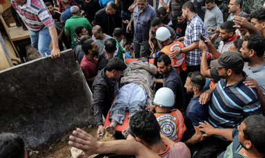 A crowd of men including rescue workers carry a man on a stretcher next to the scoop of an excavator machine