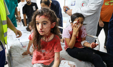 Two girls sit on a hospital bed and they have blood and bandages on them