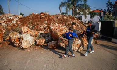 Palestinian children walk by a giant mound of red dirt and rocks that has been erected by the Israeli army