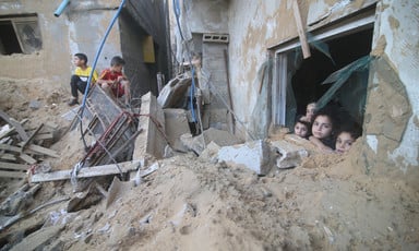 Four young children peer out of a window piled high with rubble in front of it