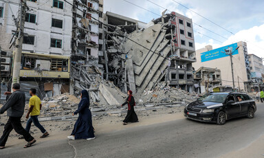 Four people walk past a building badly damaged by an Israeli air strike 